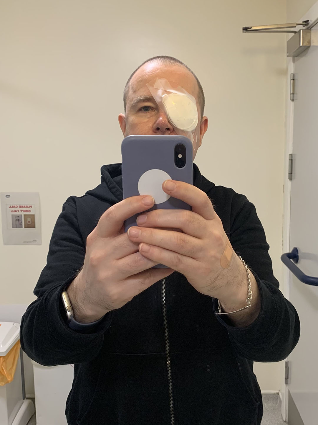 Portrait of Stewart taking a selfie in hospital with white bandages and plastic eyeguard on his right eye.