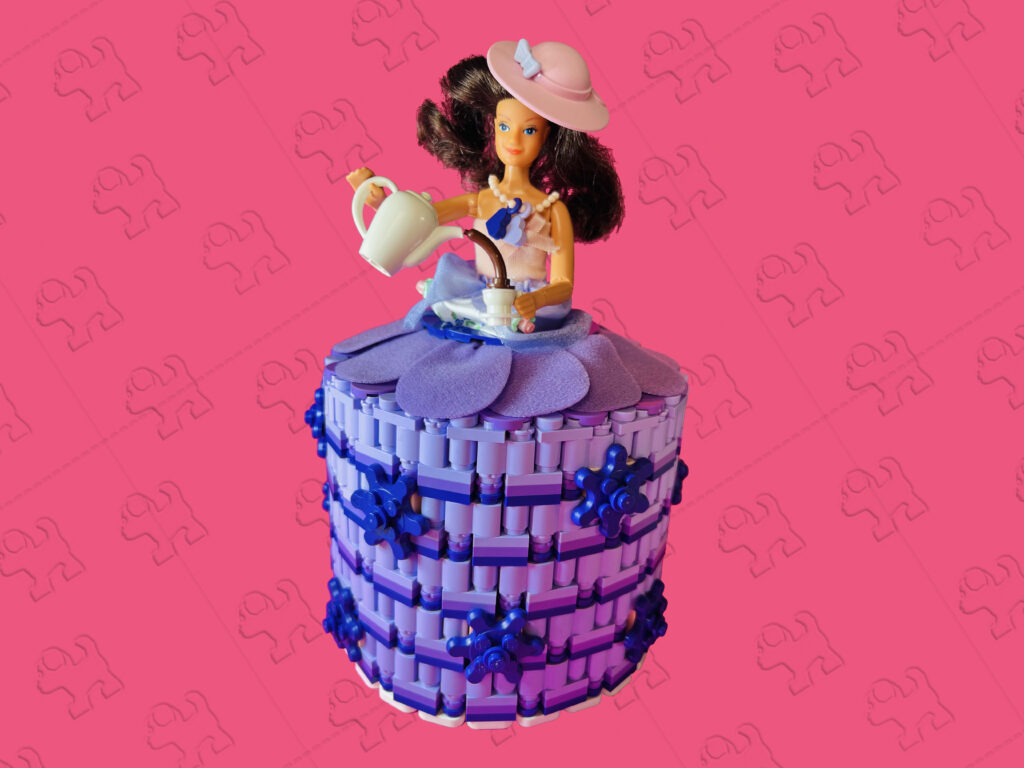 Brunette doll pouring some tea. She’s wearing a lavender, medium lavender and dark purple coloured brick-built toilet roll dress.