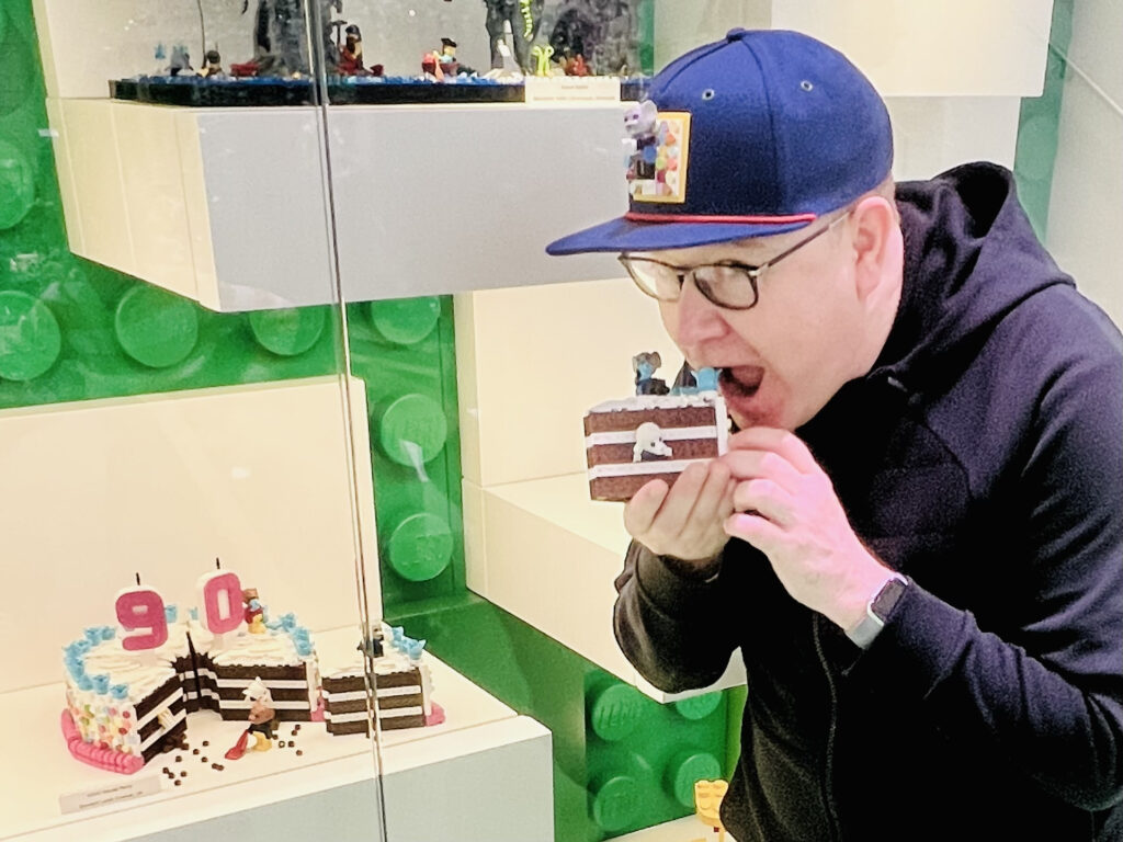 Stewart eating one slice, standing in front of an entire 90th birthday Lego cake covered in mice minifigures.