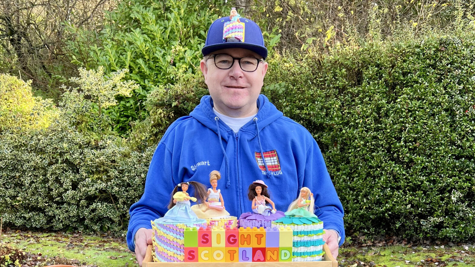 Stewart standing outside holding a tray with 4 different Lego toilet dolls on it and 'Sight Scotland' written in Duplo blocks.