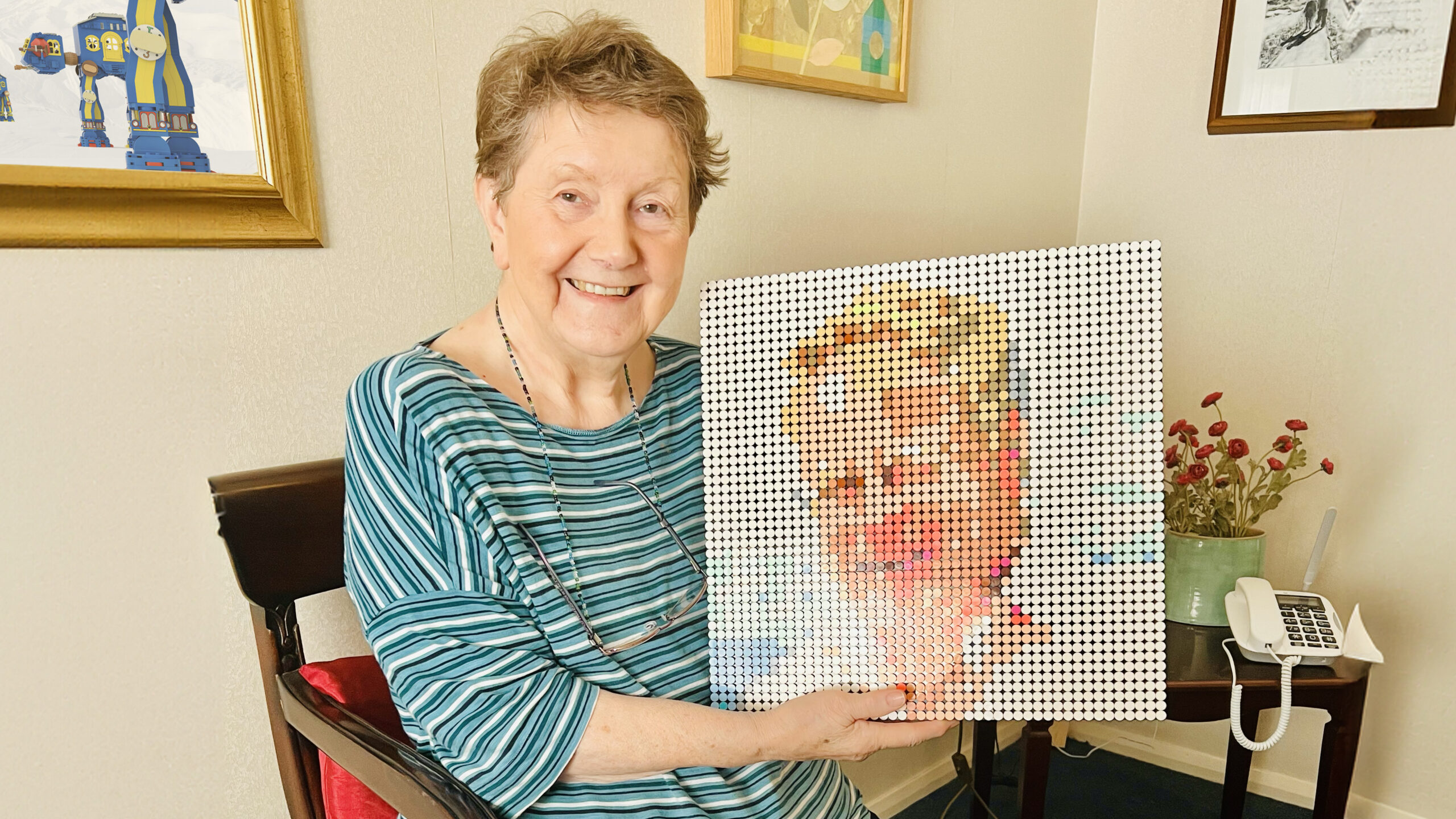 Mum sitting down, holding a large Lego mosaic of my dad's face.