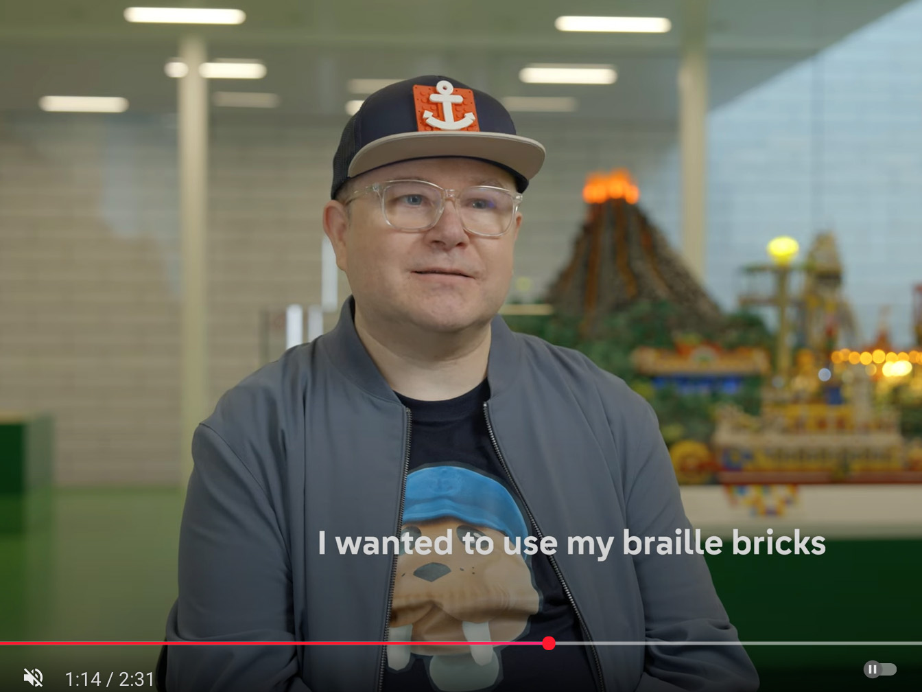 Stewart inside the Lego House wearing a Captain’s cap (brick-built anchor), with the subtitles ‘I wanted to use my Braille bricks’.