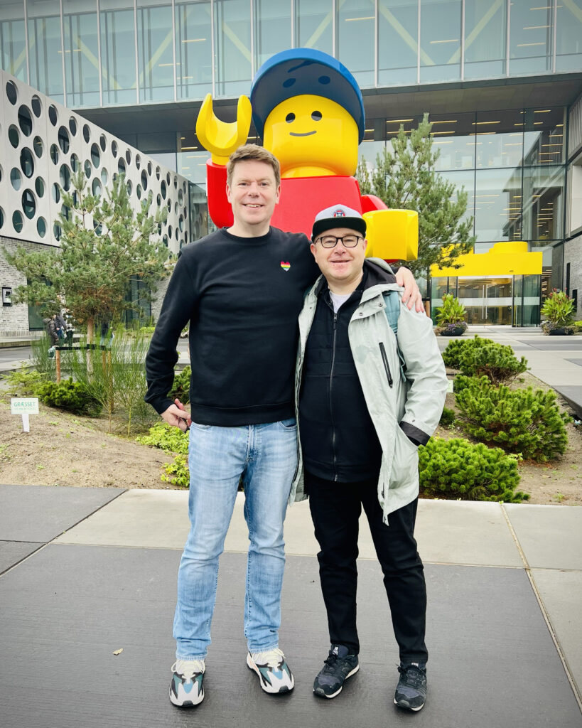 Stewart and Peter standing in front of a giant Minifigure sculpture outside Lego Campus, Billund.