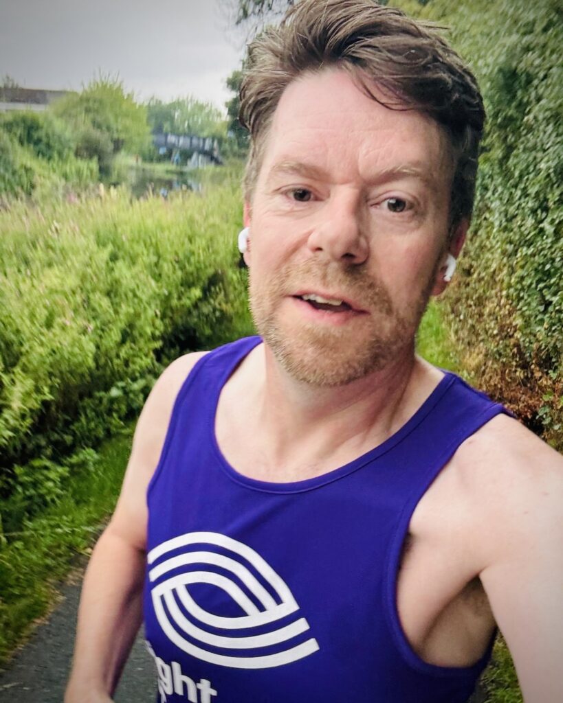 Peter wearing a Sight Scotland vest during a training run alongside a grassy canal bank.